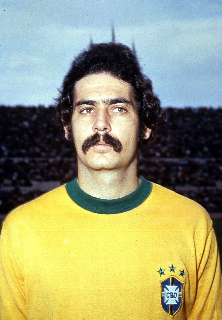Rivelino in Brazil’s 1970 World Cup uniform, standing in front of a crowded stadium, wearing a yellow jersey with green trim.